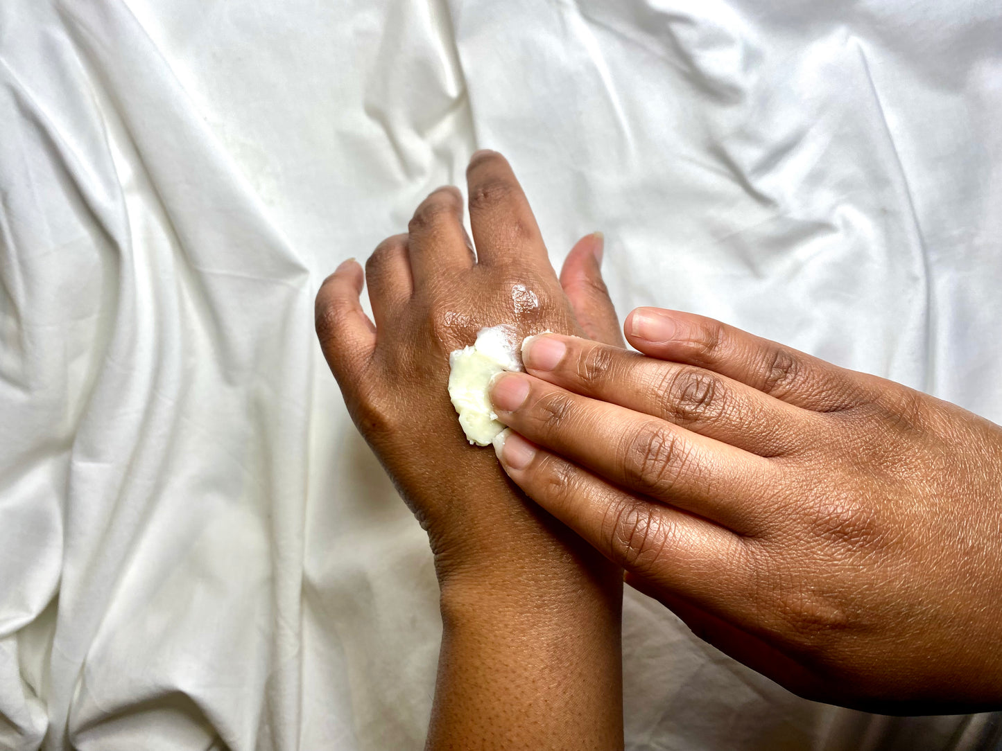 Two hands applying cream to a white sheet